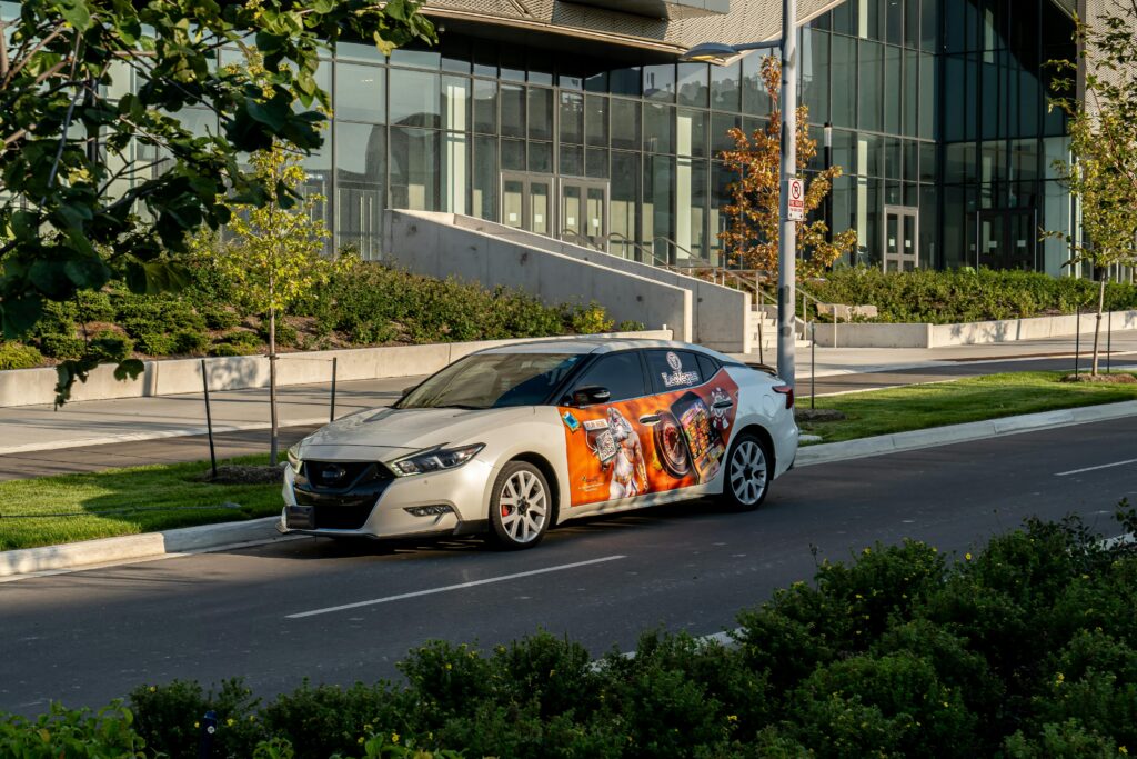 A modern car with vibrant advertising wrap parked on a city street next to a contemporary building.